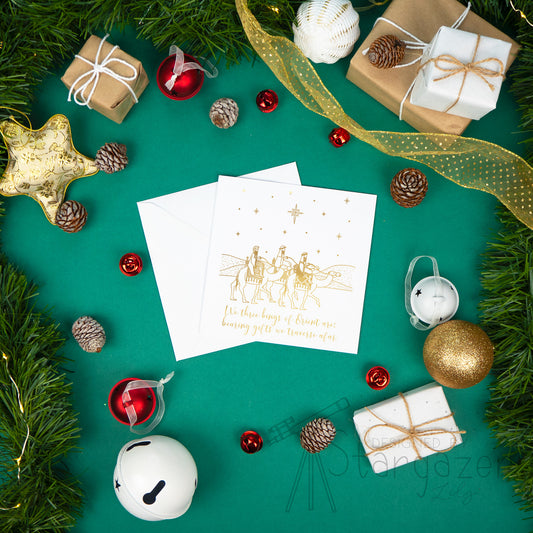 Minimalist gold foil line art Christmas card featuring the three wise men riding camels beneath the Christmas star and the lyrical quote "We three kings of Orient are; bearing gifts we traverse afar" on a square card